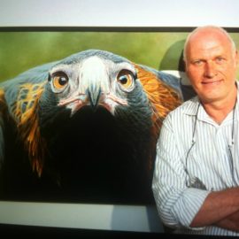 Artist Tony Pridham standing in front of a large painting of a Wedge-tailed eagle